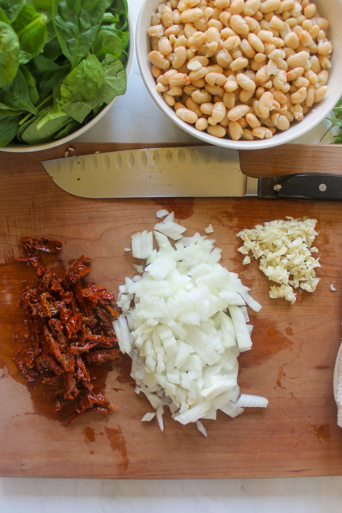 Chopped onion, garlic, and sun-dried tomato on a cutting board.