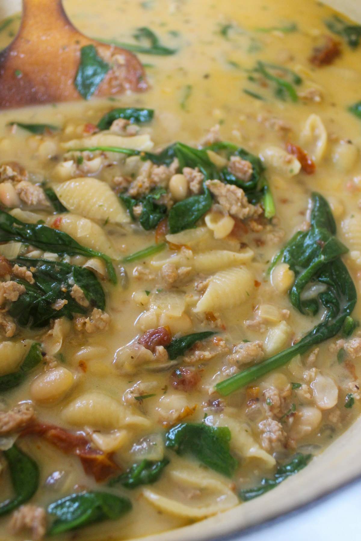 A pot of creamy soup with sausage, spinach, and pasta shells.