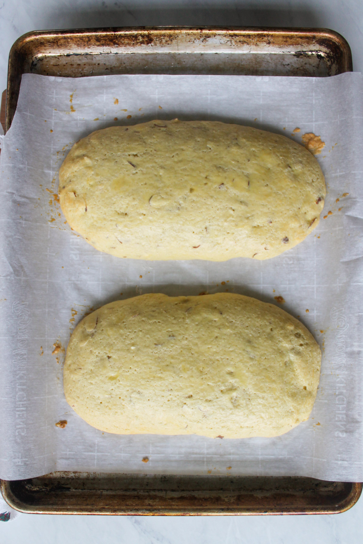 Two baked loaves of almond biscotti on a sheet pan.