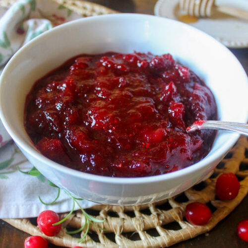 A white bowl of cranberry sauce with a spoon.