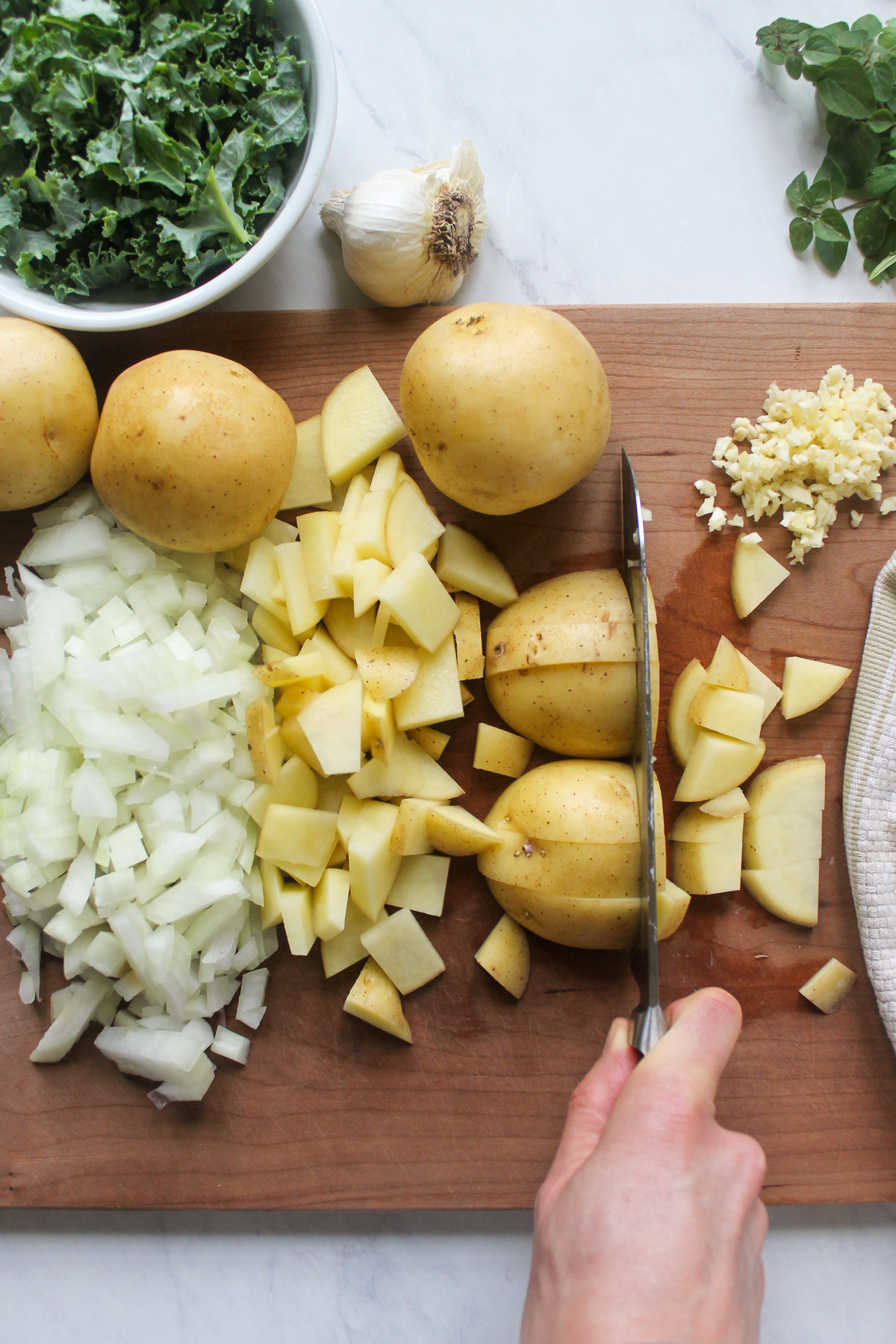 Slicing potatoes on a cutting board with chopped onions.