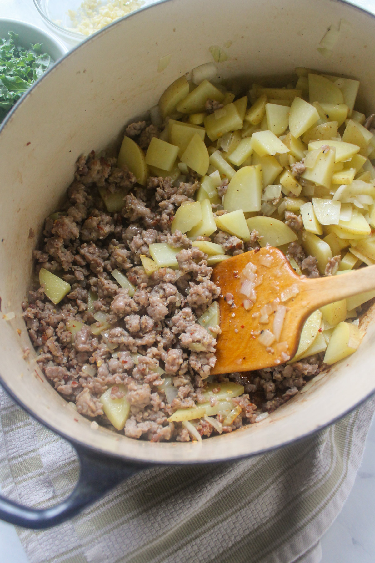 A soup pot with browned sausage on one side and chopped onions and potatoes on the other.