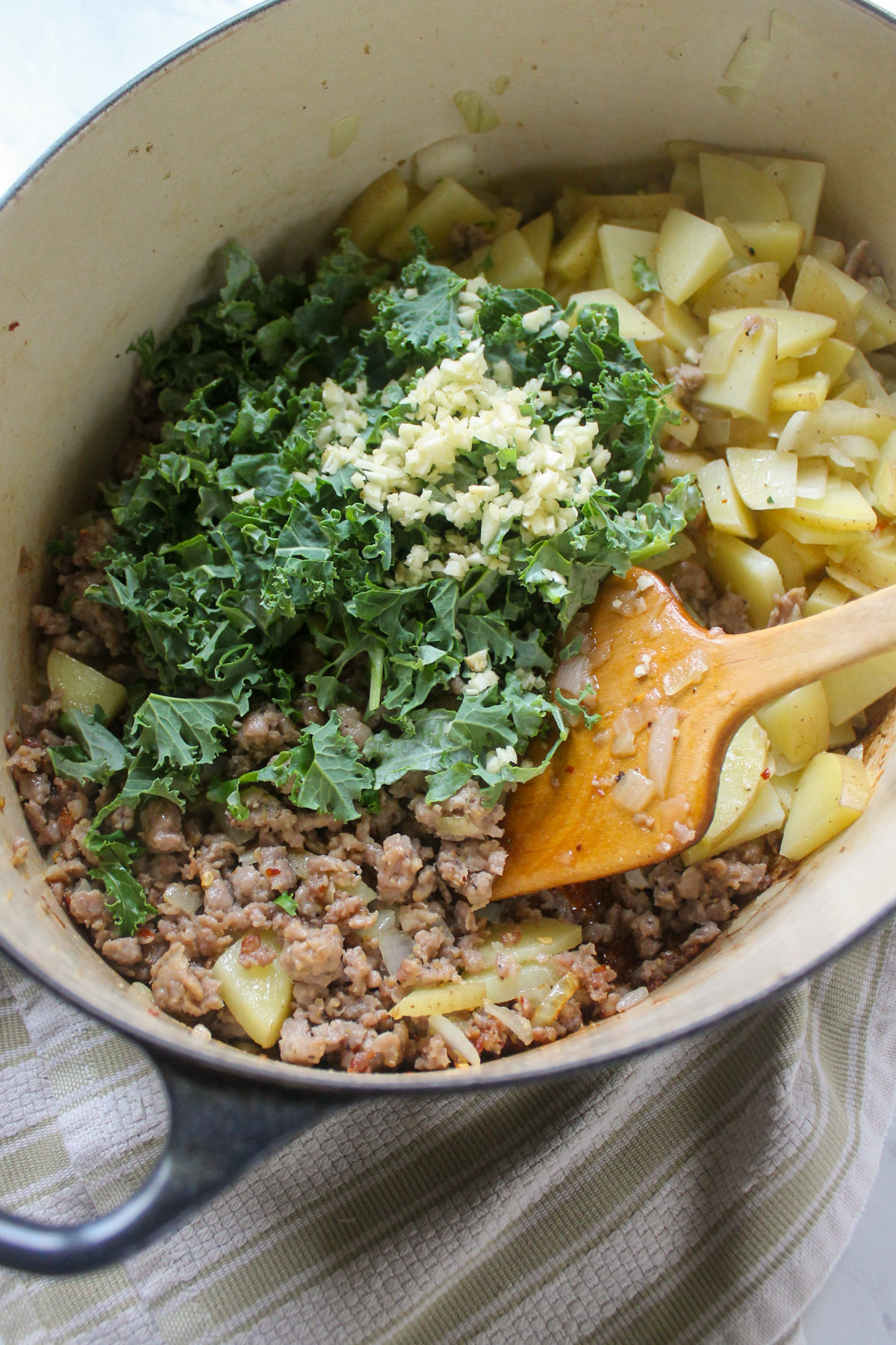 Adding kale and garlic to cooking sausage and potato soup.