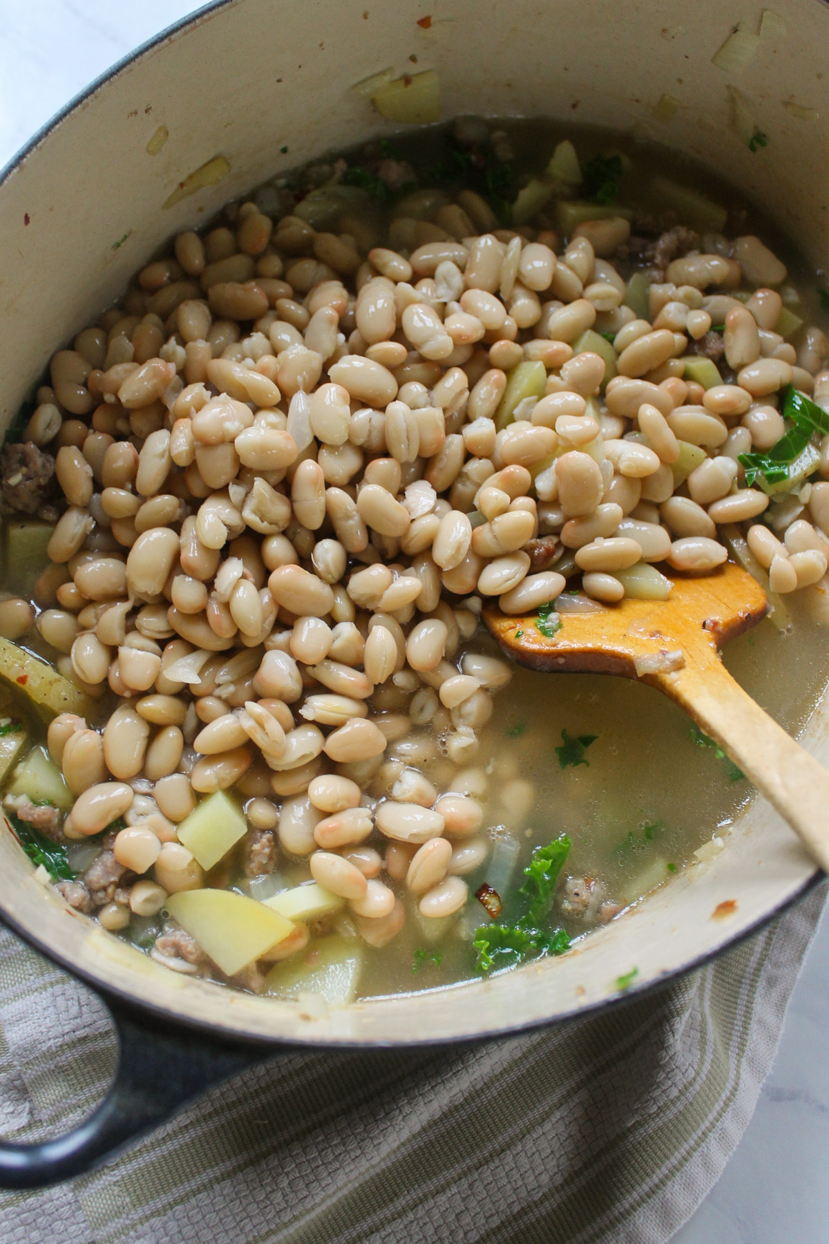 Adding white beans and chicken stock to soup.