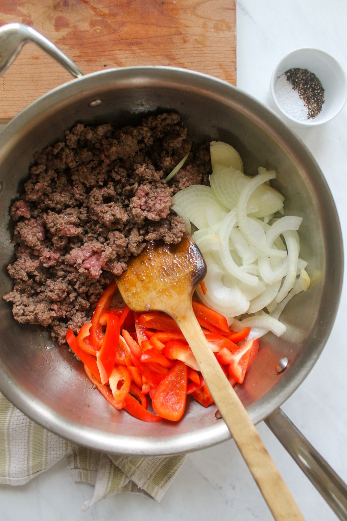 A skillet with ground beef browning alongside red peppers and onions.