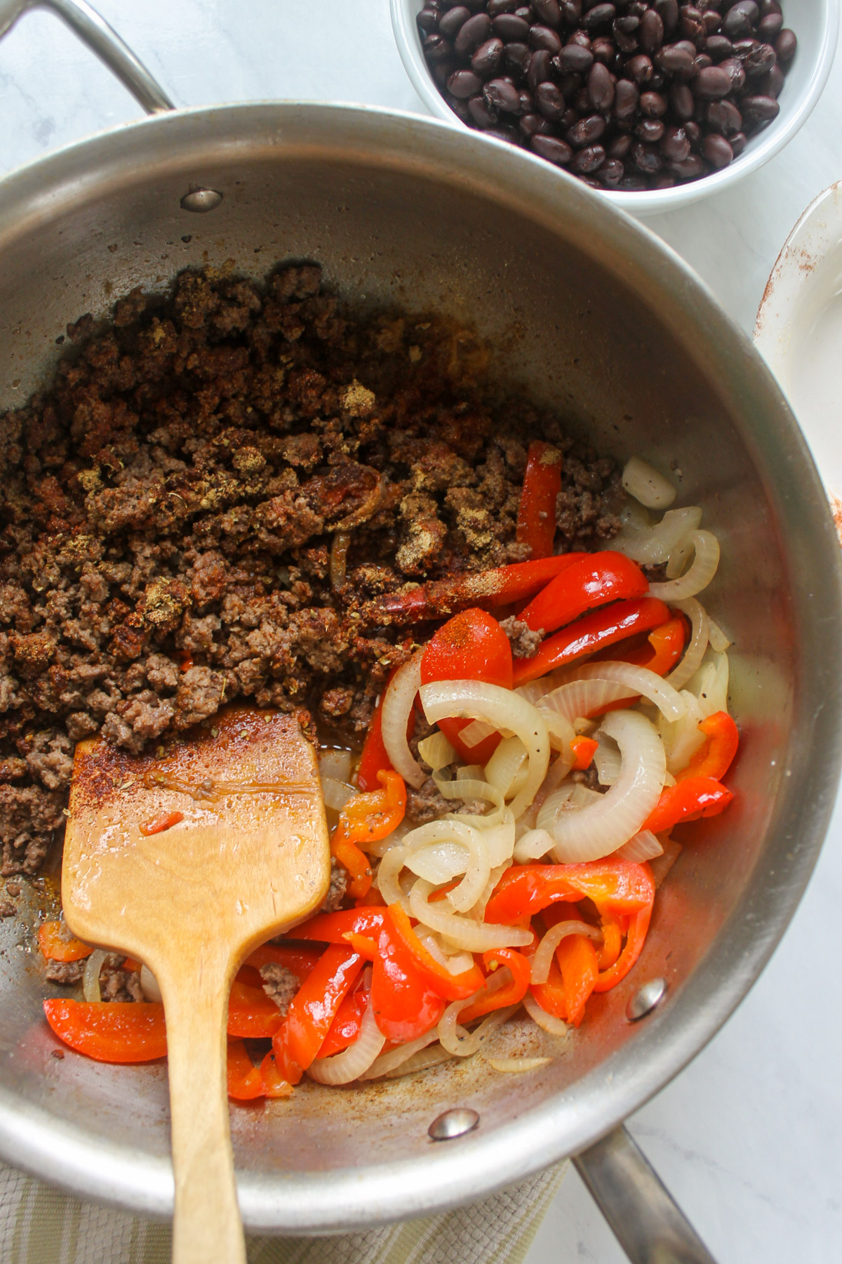 Adding spices to ground beef in a skillet with red peppers and onions.