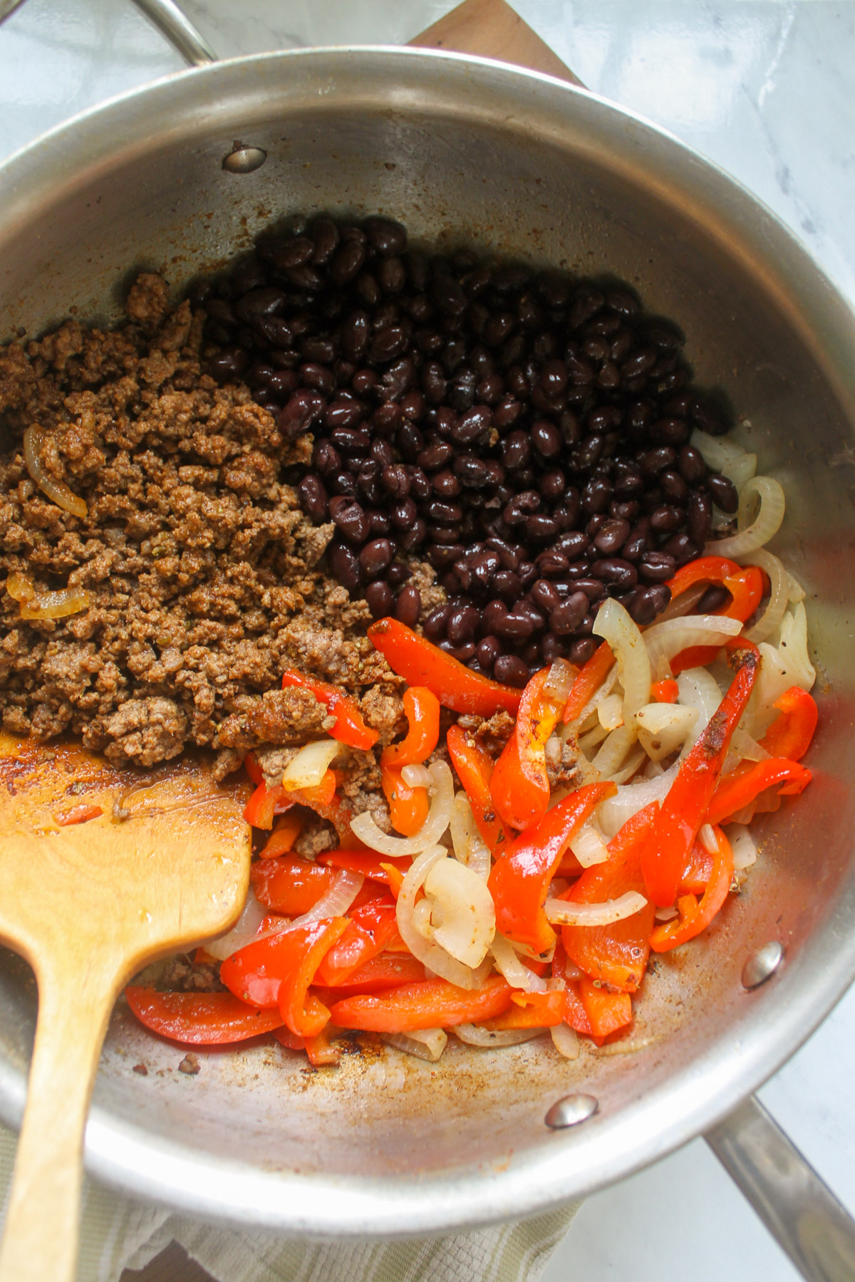 Cooking ground beef, peppers, onions and beans in a skillet.