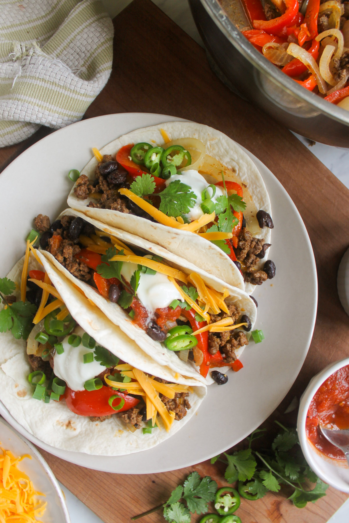 Beef fajita tacos on a plate with salsa, scallions, cilantro and cheese.