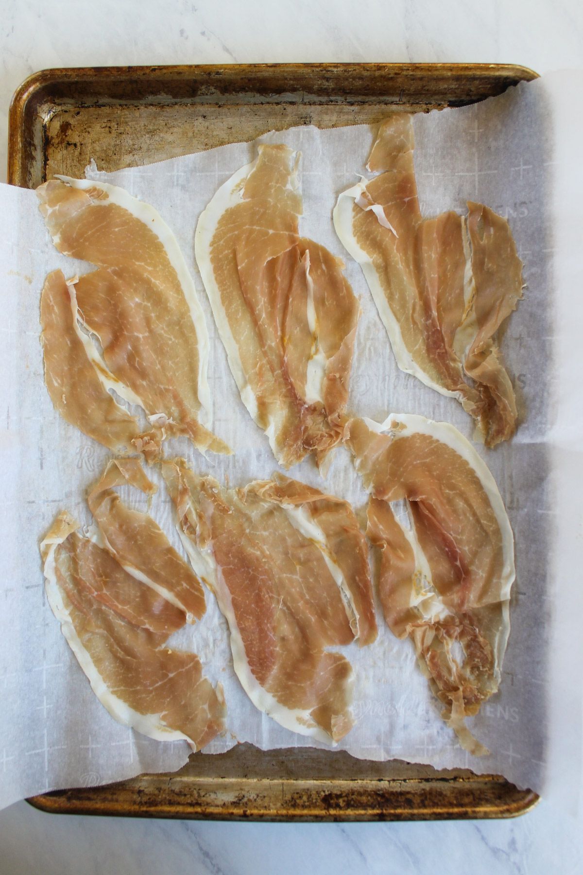 Six slices of prosciutto on a sheet pan with parchment paper.