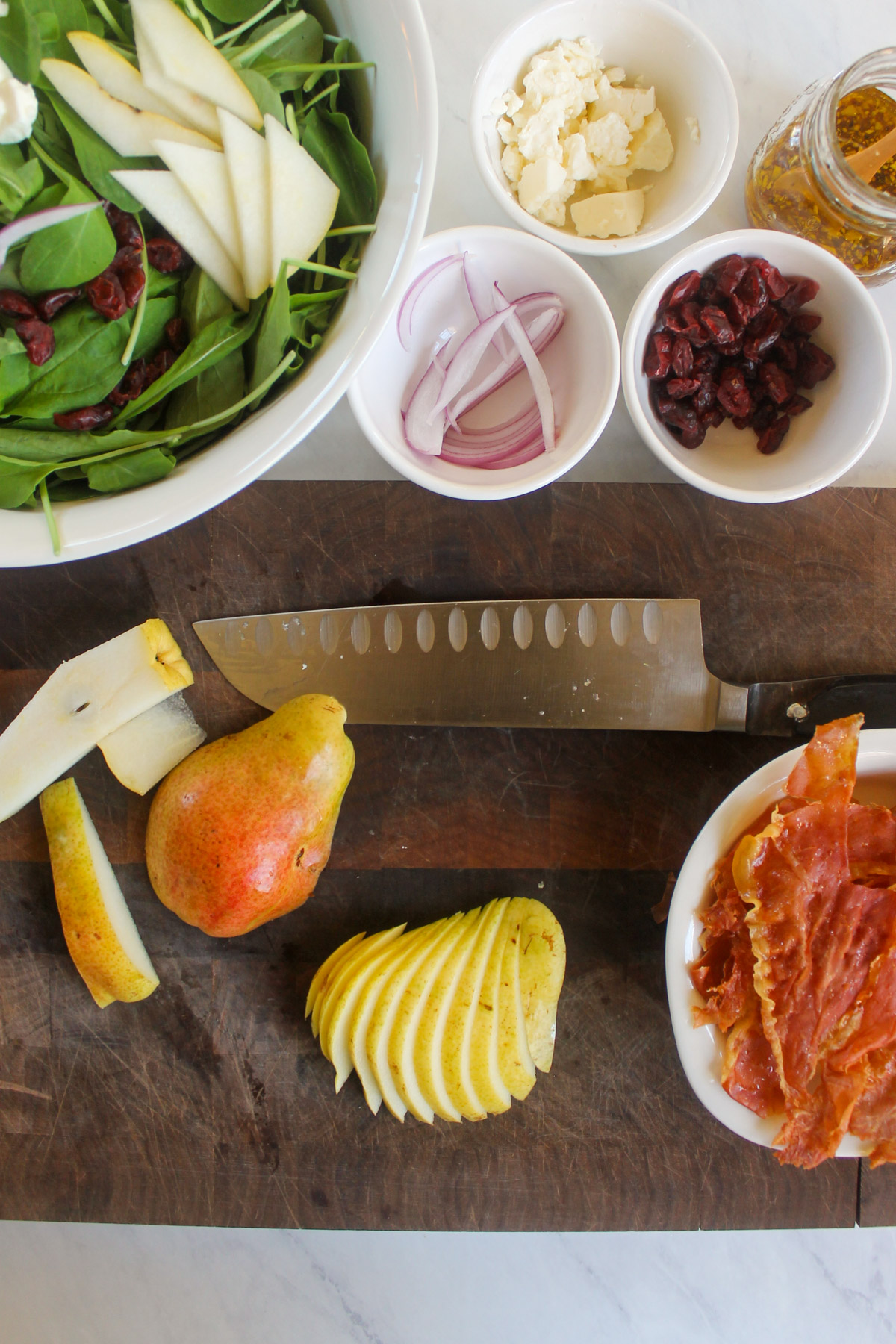 A sliced pear on a cutting board with a bowl of salad and crispy prosciutto.