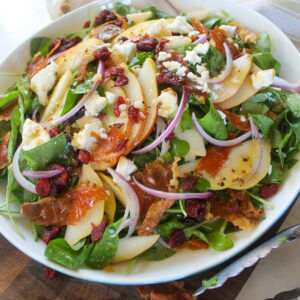 A salad with sliced pears, crispy prosciutto, arugula, red onion, feta and craisins.