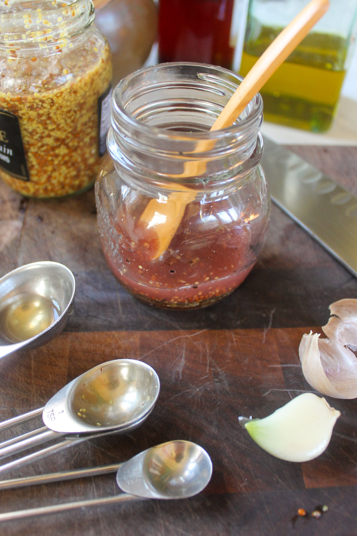 Making a jar of honey red wine vinaigrette on a cutting board with garlic.