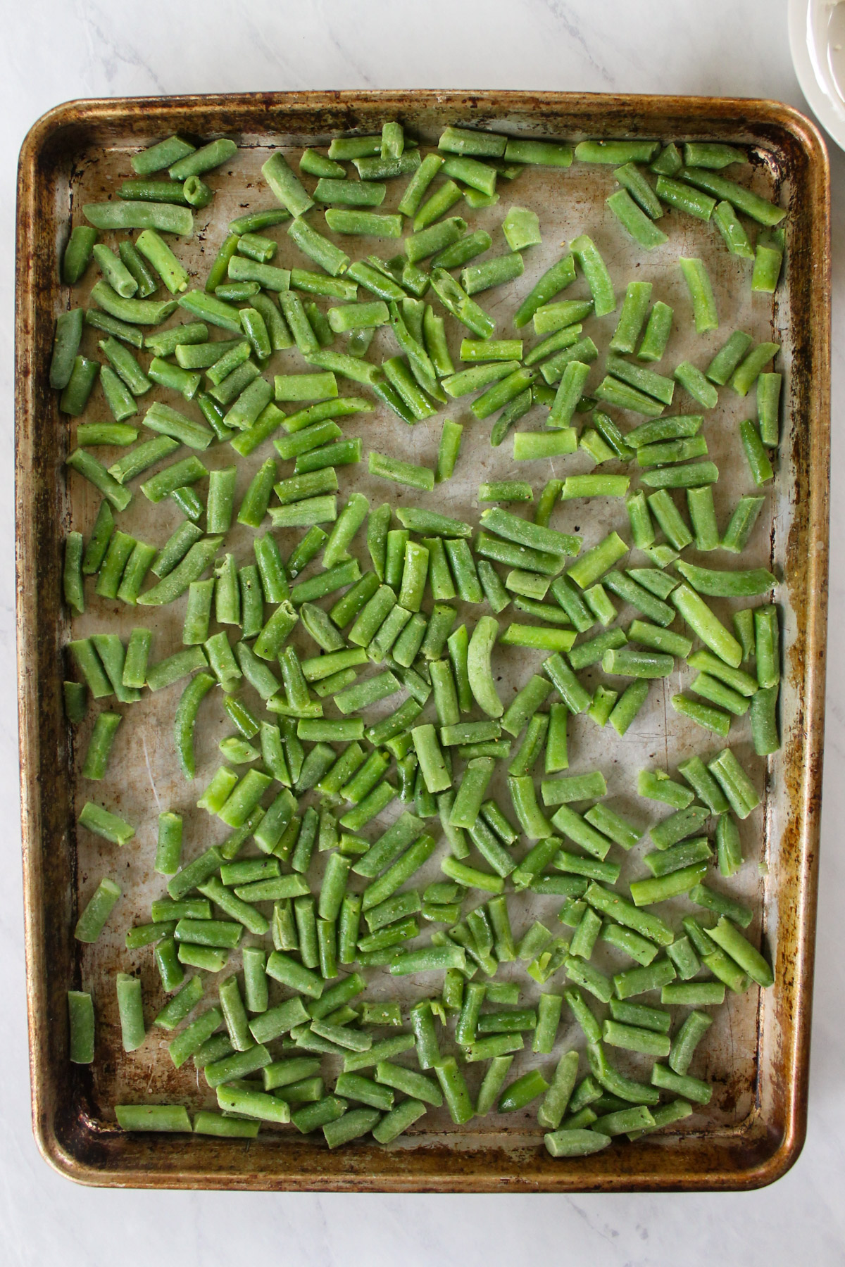 A sheet pan of frozen green beans tossed with olive oil, salt and pepper.