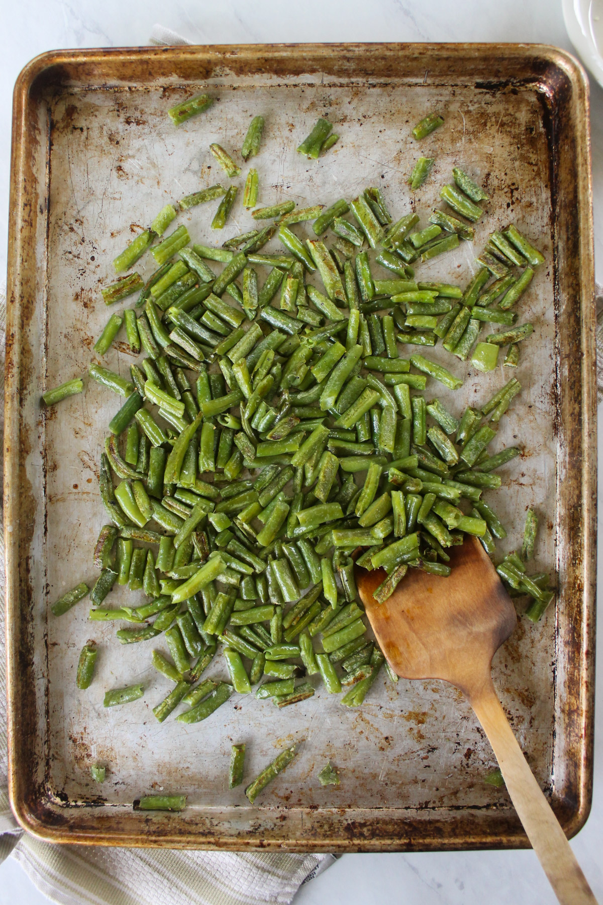 A sheet pan of roasted frozen green beans with a wooden spoon.