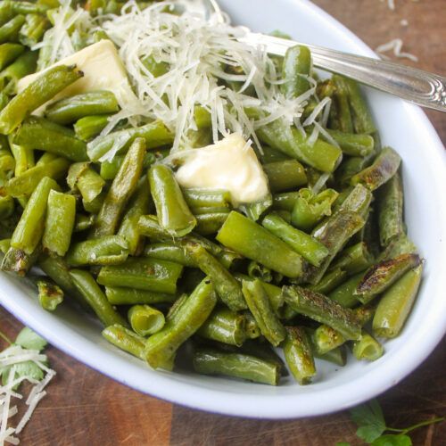 A white bowl of roasted frozen green beans with a spoon.