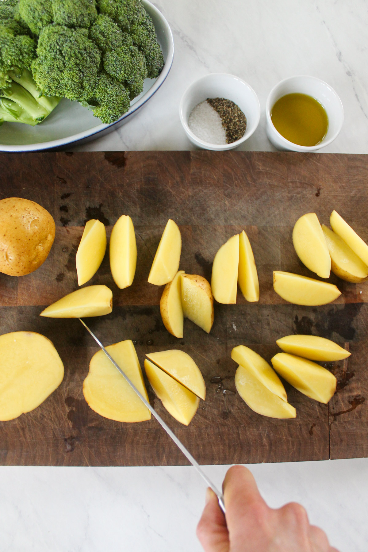 Chopping potatoes into wedges on a cutting board.