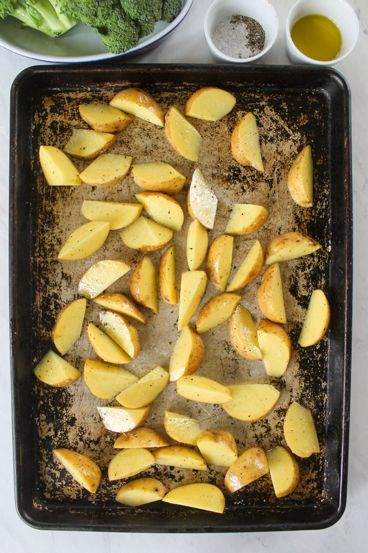 Raw chopped potatoes withe olive oil, salt and pepper on a baking sheet.