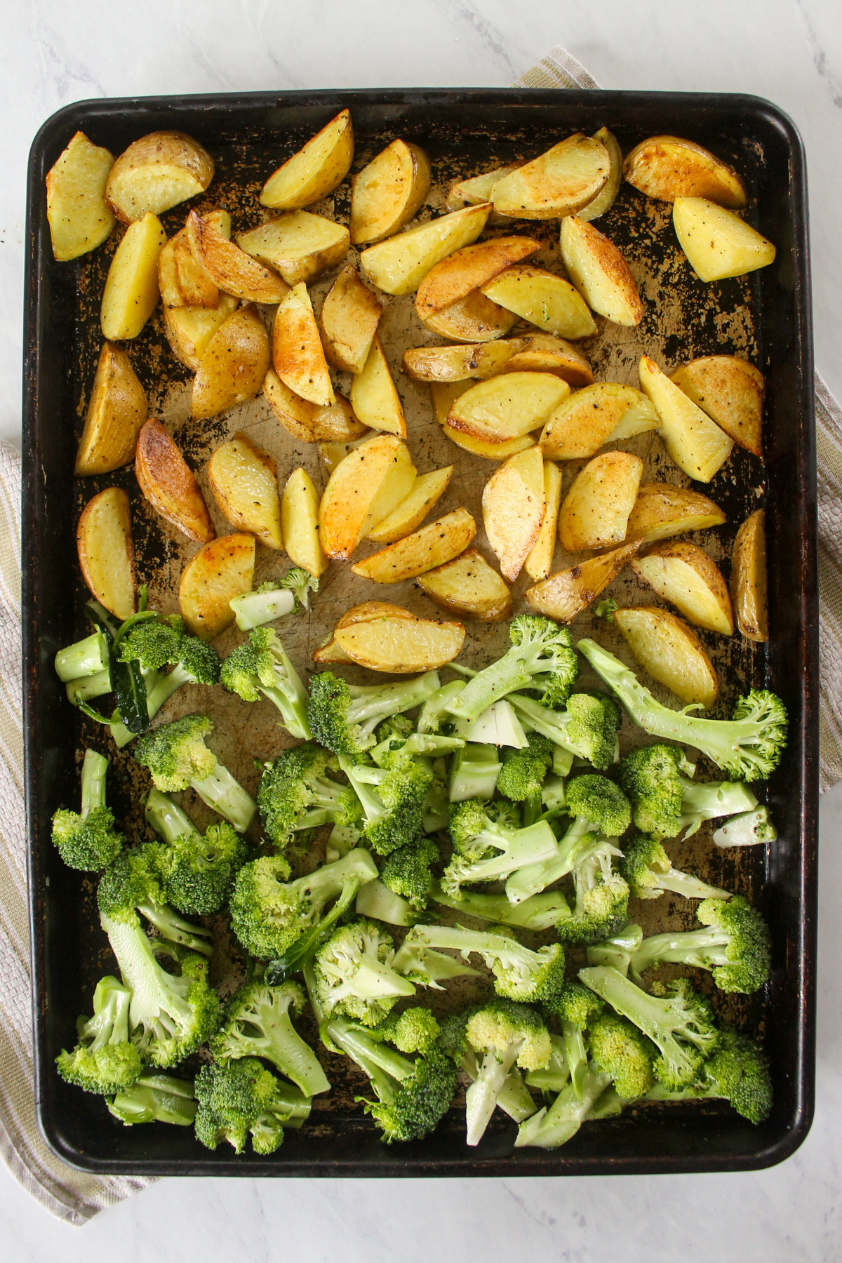 Roasted potatoes on half a baking sheet with raw broccoli added to the other half.