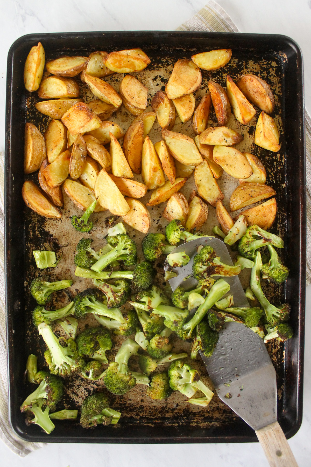 A sheet pan with half roasted potatoes and half roasted broccoli.