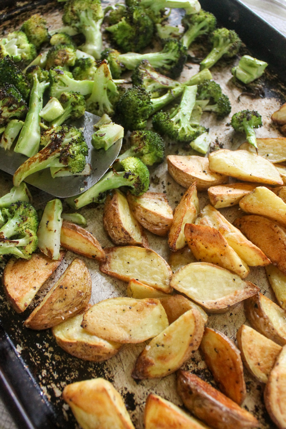 Roasted potato wedges and broccoli florets on a pan.