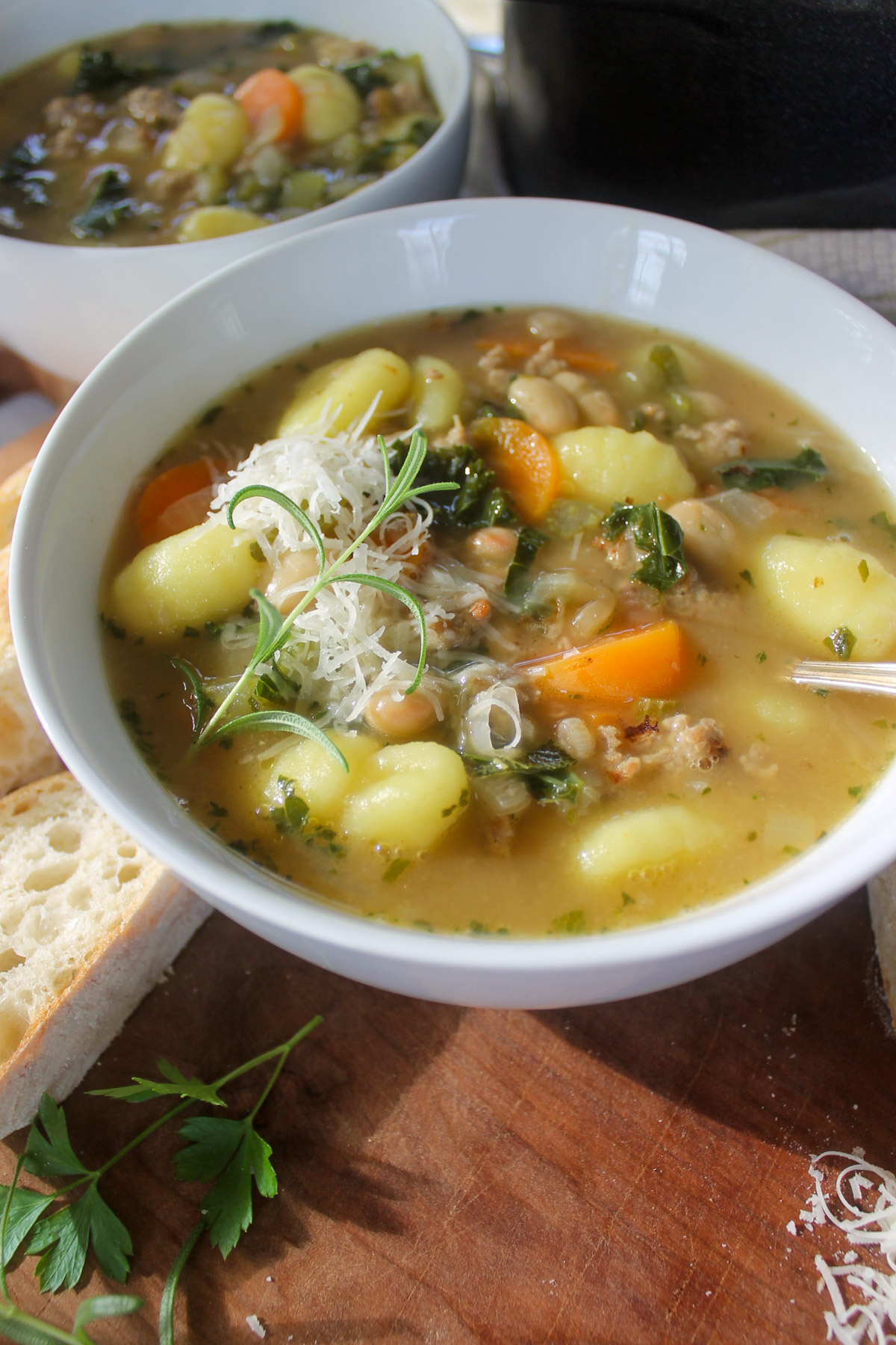 A white bowl of soup with gnocchi, sausage and carrots in broth.