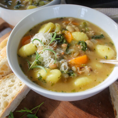 A bowl of soup with sausage, gnocchi, carrots, and kale.