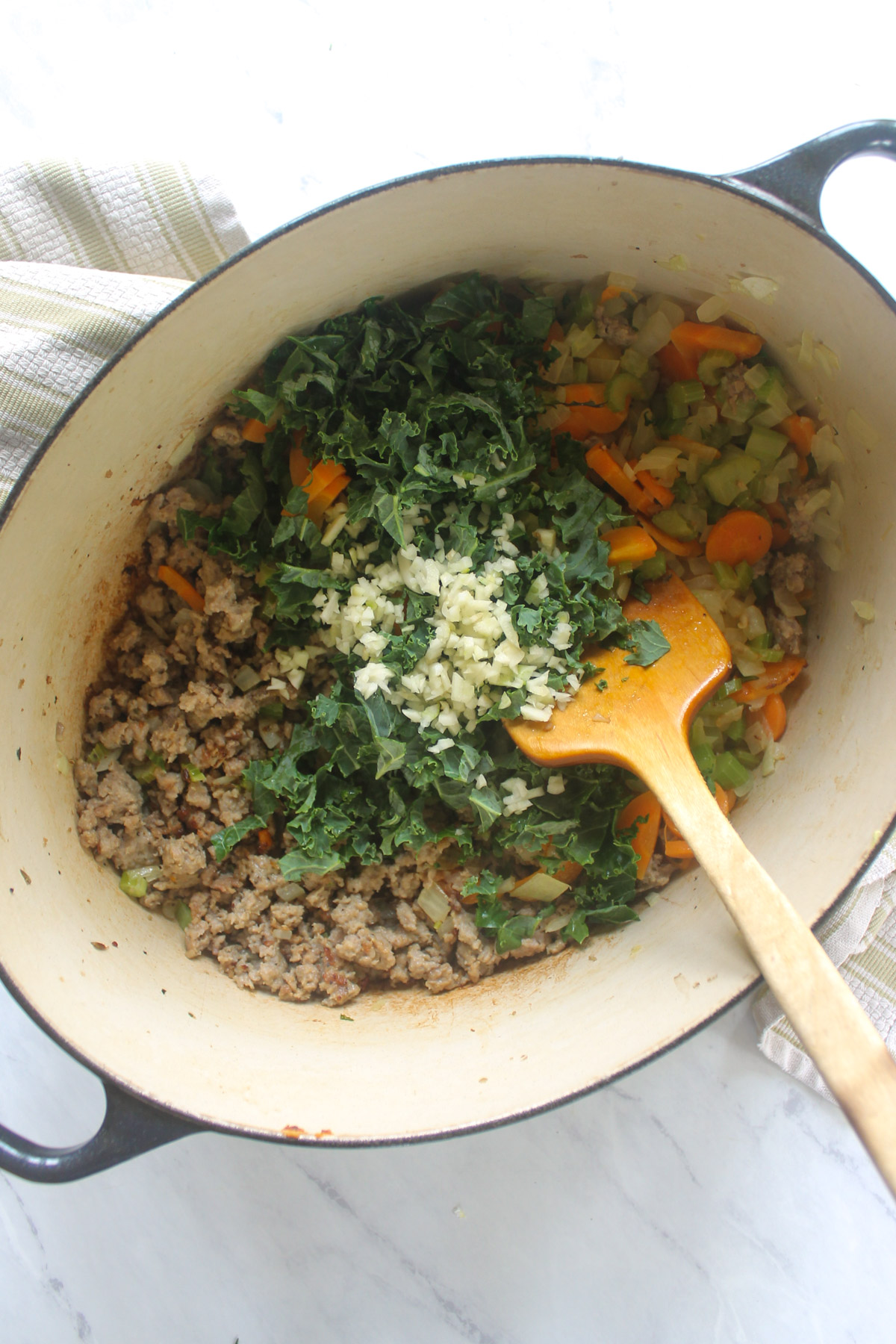 A soup pot with cooked sausage and veggies with kale and garlic added.