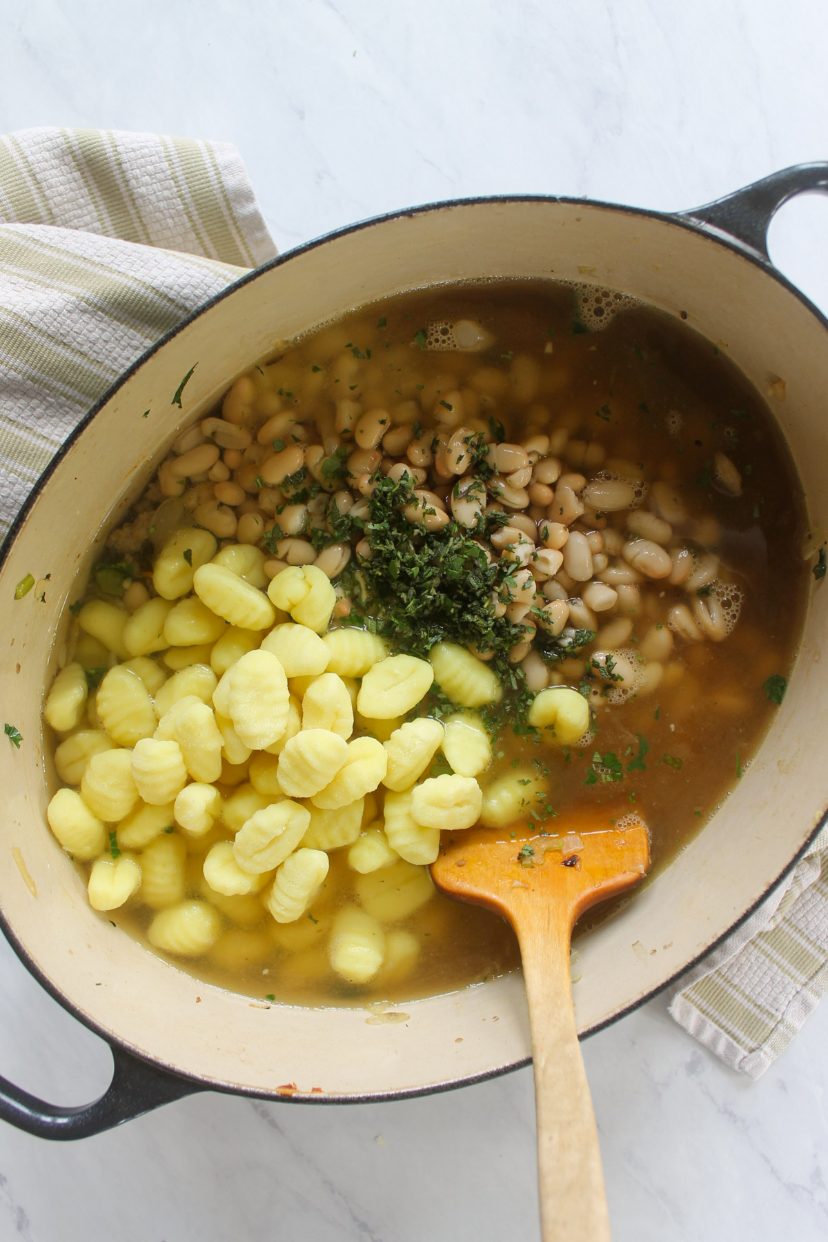 Adding white beans, herbs and potato gnocchi to a pot of soup.