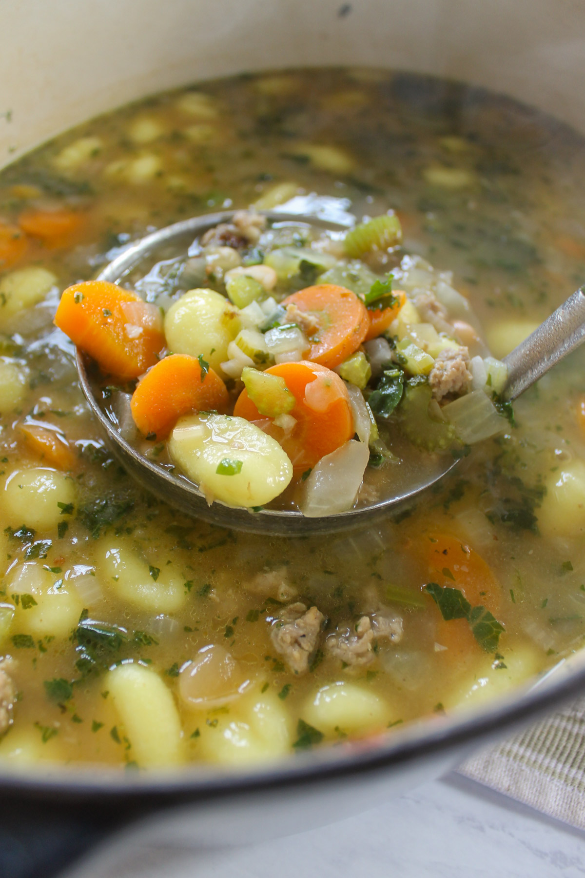 A ladle full of sausage gnocchi soup with carrots.