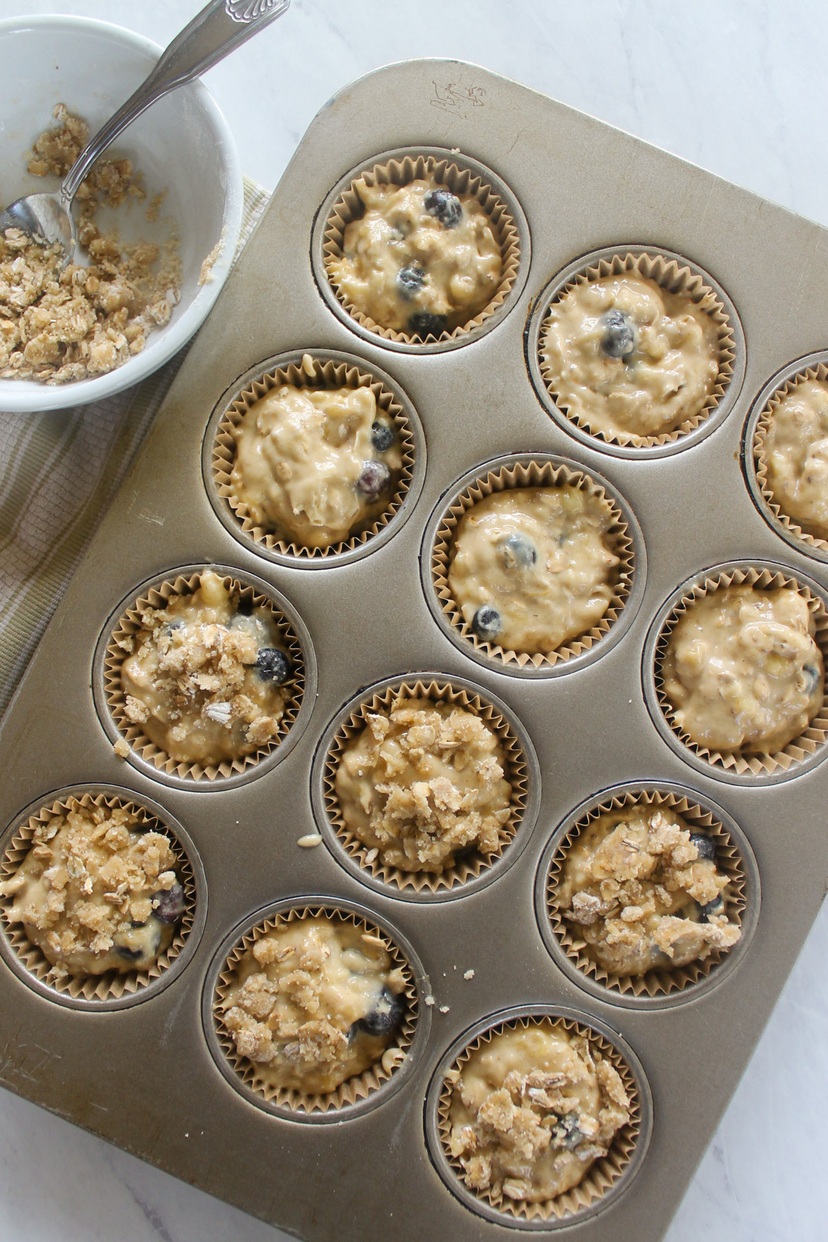 Banana blueberry muffin batter in a lined muffin pan, adding topping.