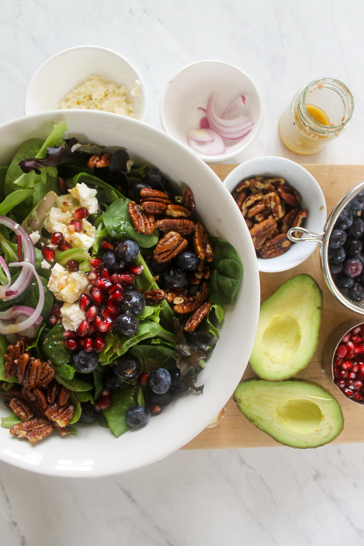 A bowl of salad ingredients with lettuce, blueberries, pomegranate seeds, pecans and feta cheese.