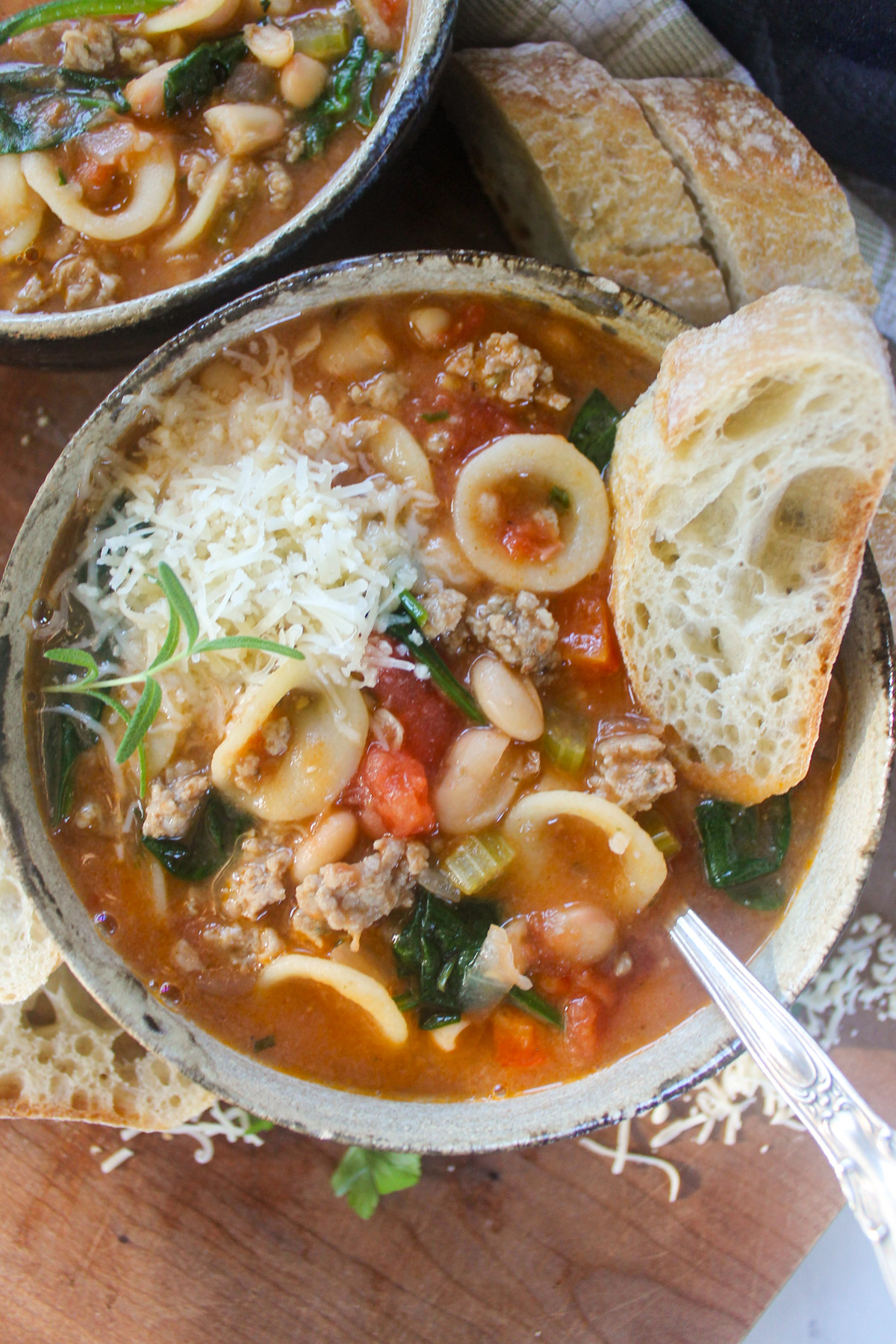 A bowl of sausage tomato pasta soup with bread.