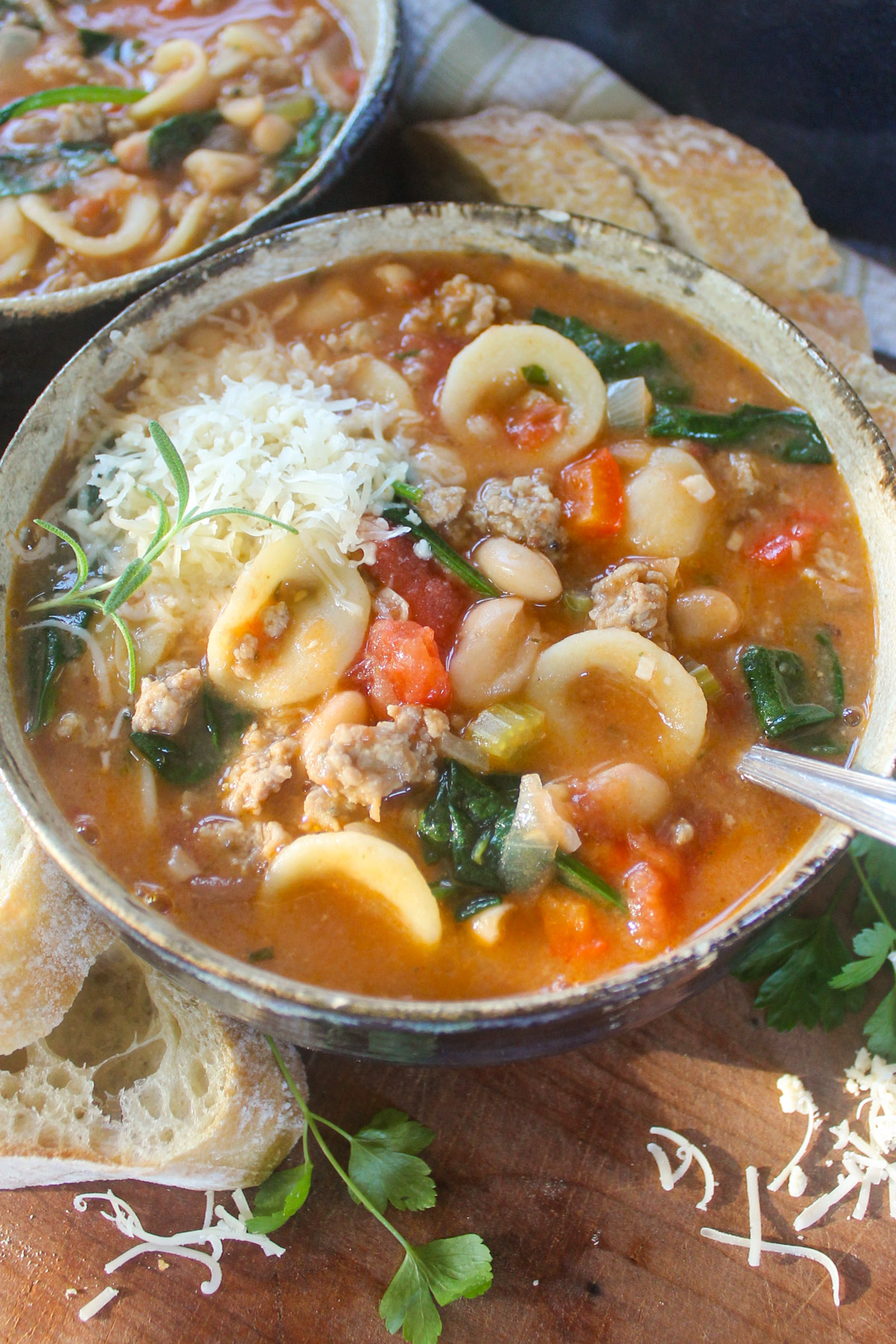 A bowl of Italian sausage white bean soup with pasta and Parmesan cheese.