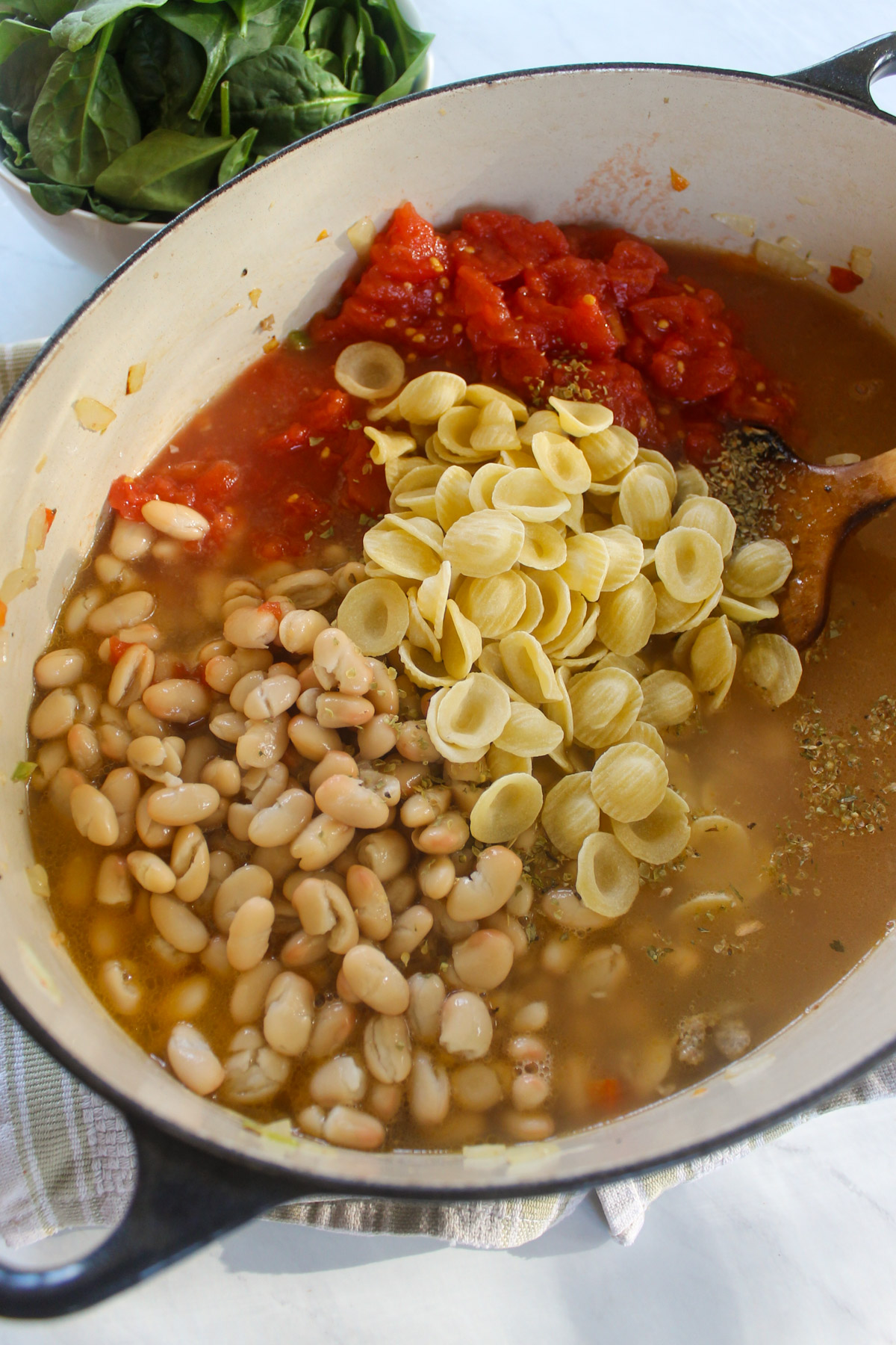 Adding white beans, dry pasta, tomatoes and stock to soup.