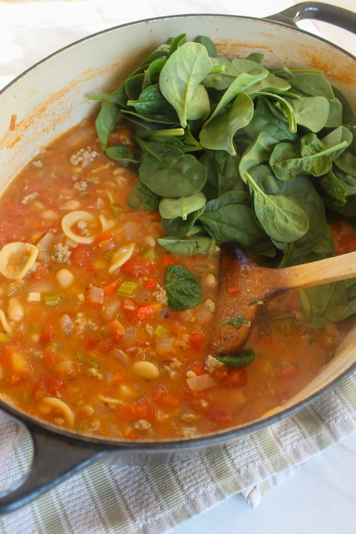 Adding fresh spinach to a pot of tomato pasta soup.