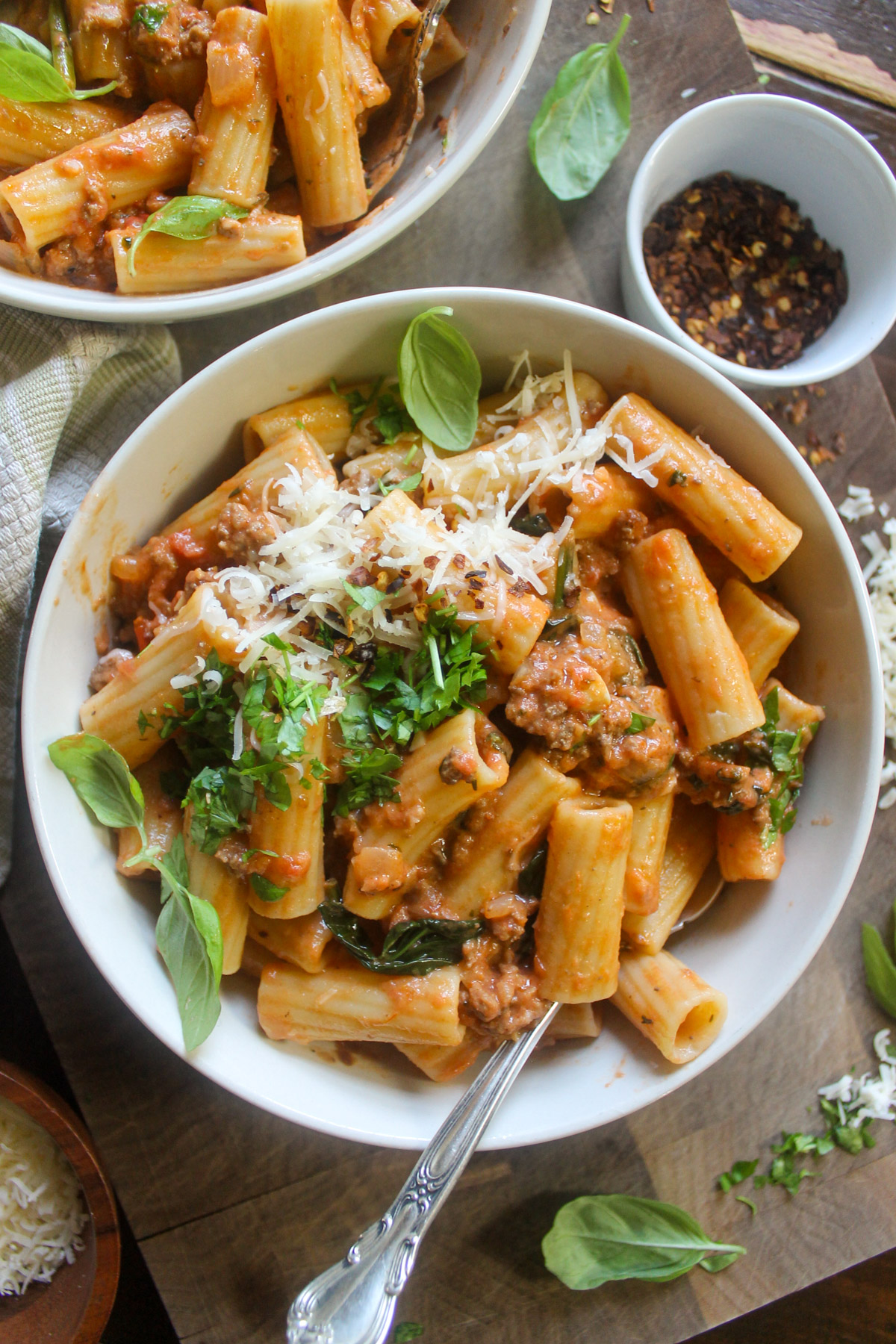 A bowl of spicy rigatoni with meat sauce topped with cheese, basil and crushed red pepper flakes.