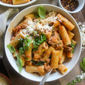 A bowl of rigatoni pasta with tomato meat sauce and spicy crushed red pepper flakes.