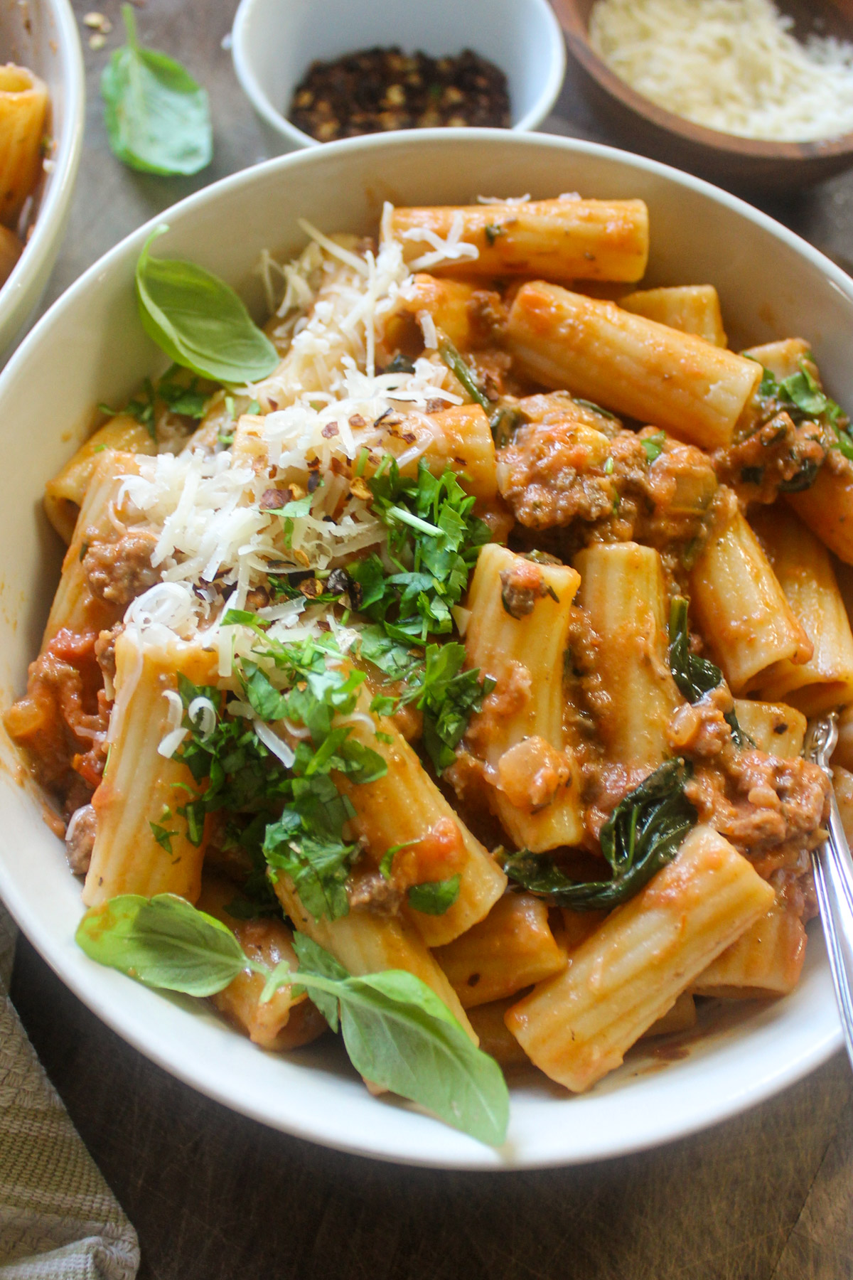 A bowl of rigatoni pasta with red meat sauce and spicy red pepper flakes with basil and Parmesan.