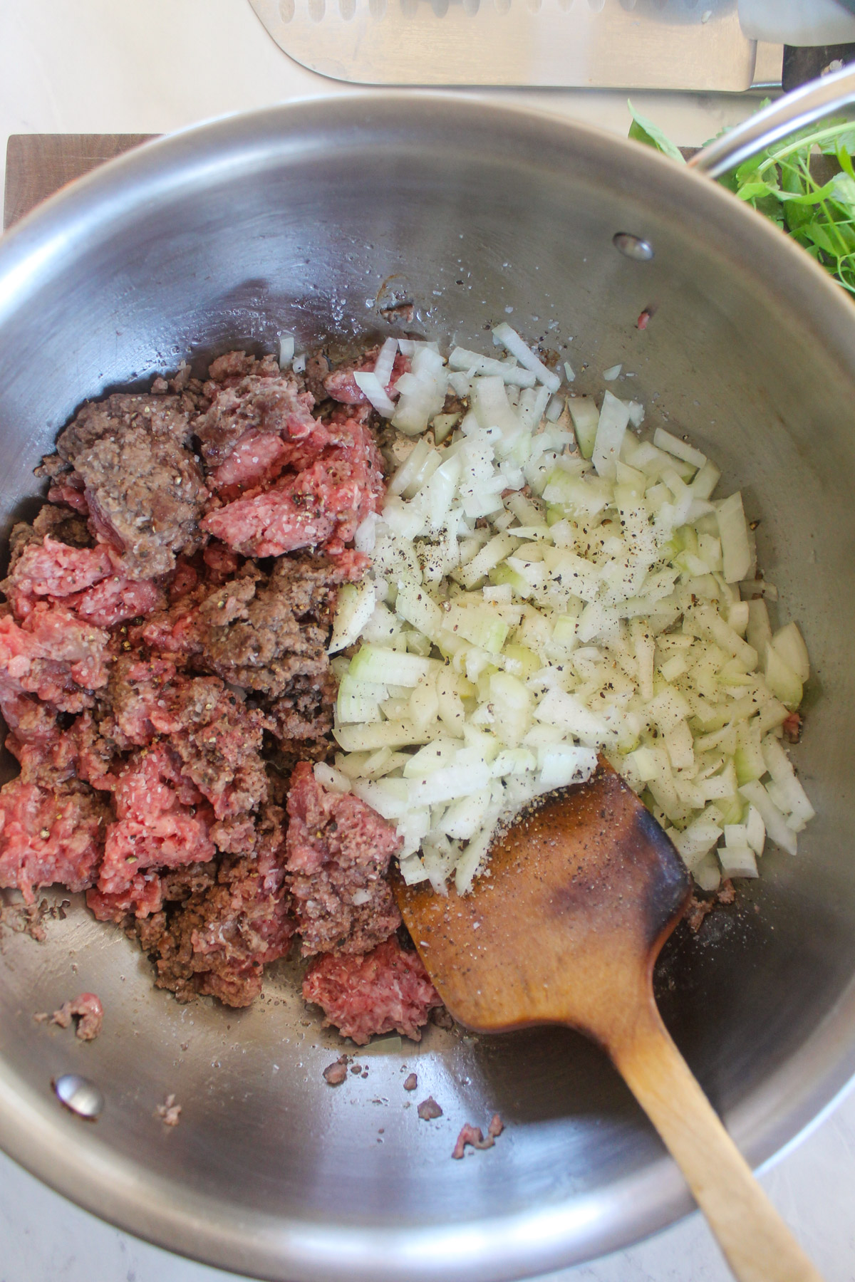 Onions and ground beef cooking on each half of a skillet.