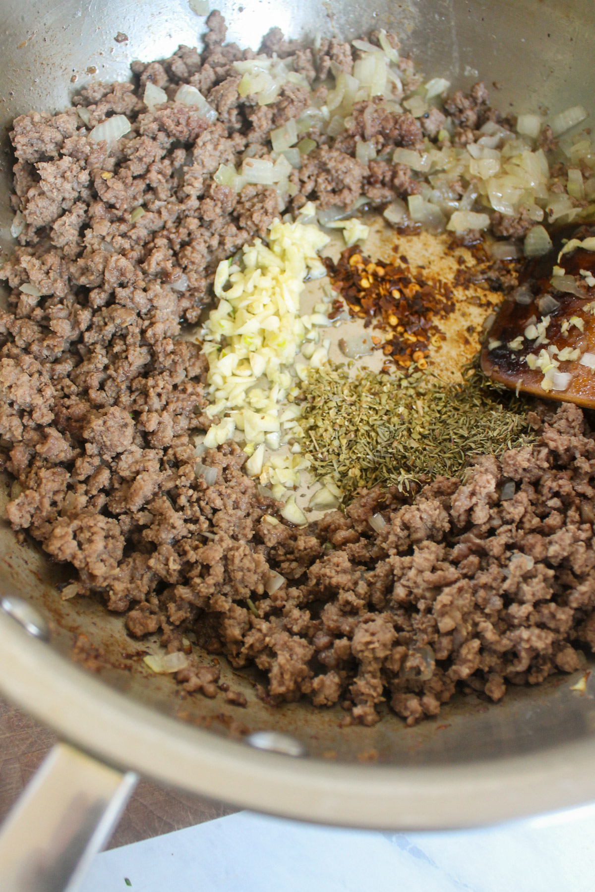 Adding garlic, crushed red pepper flakes and dried spices to the skillet with ground beef and onions.