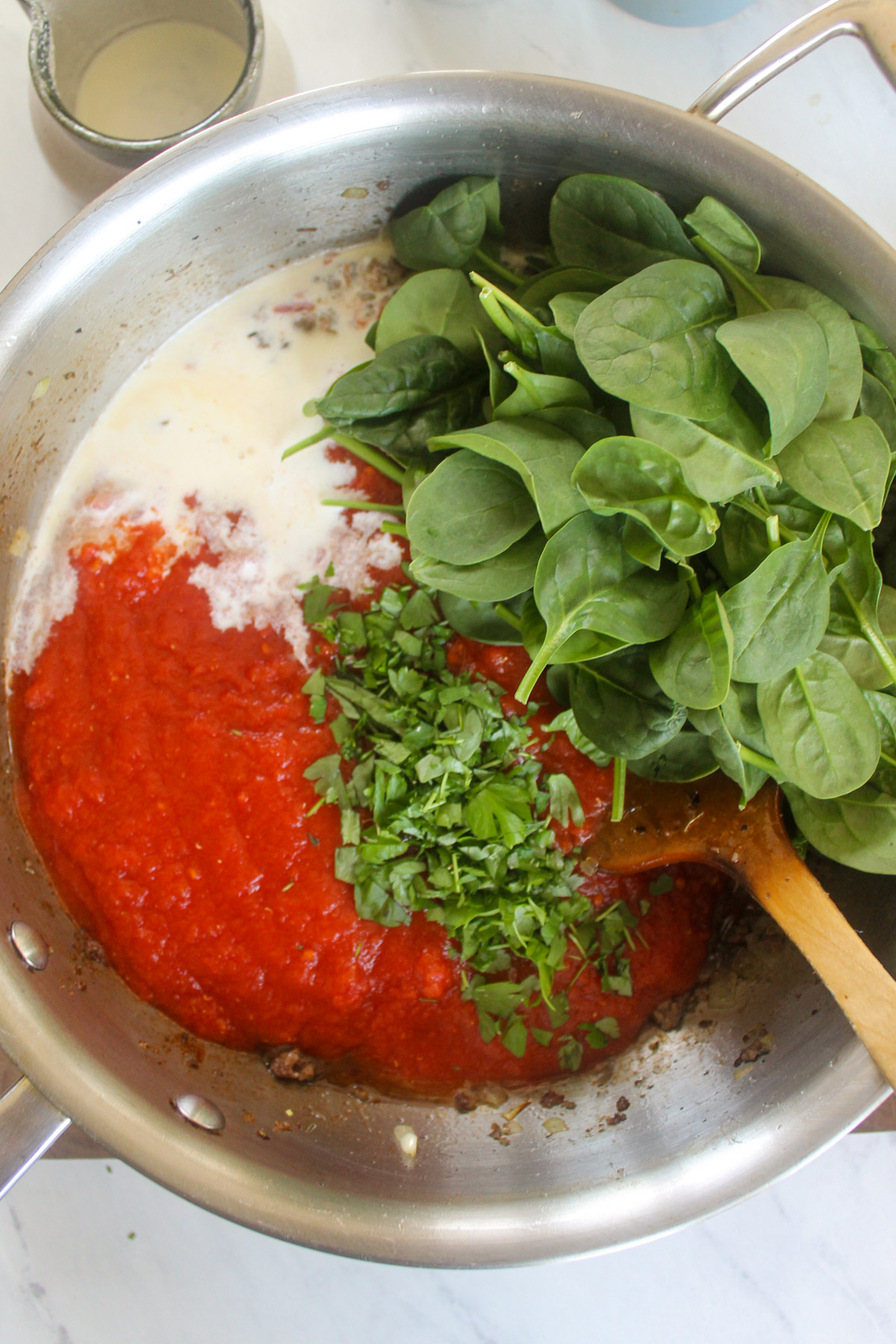 Adding canned tomato, cream and fresh spinach to a skillet of meat sauce.