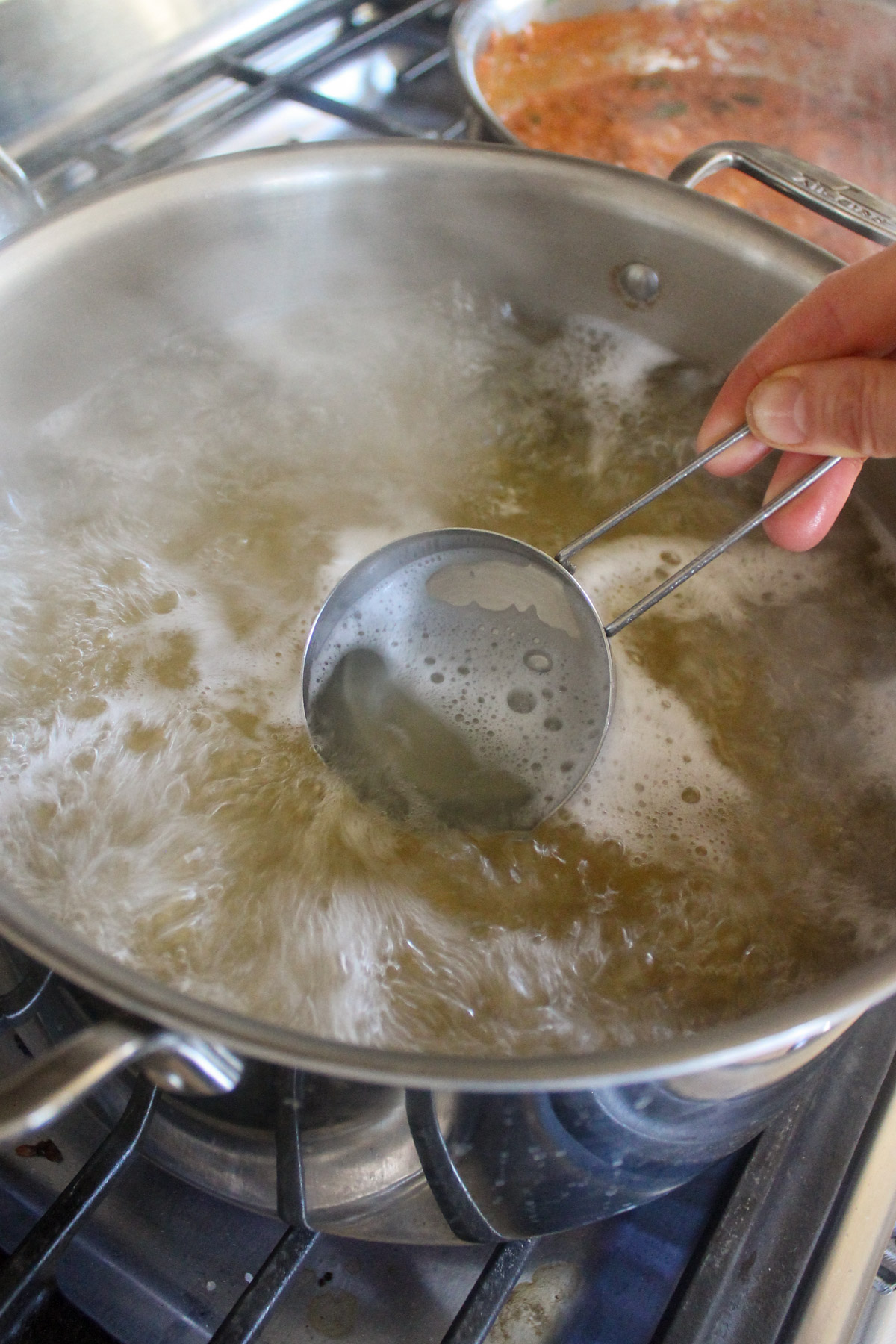 Scooping starchy cooking water out of a boiling pot of pasta with a measuring cup.