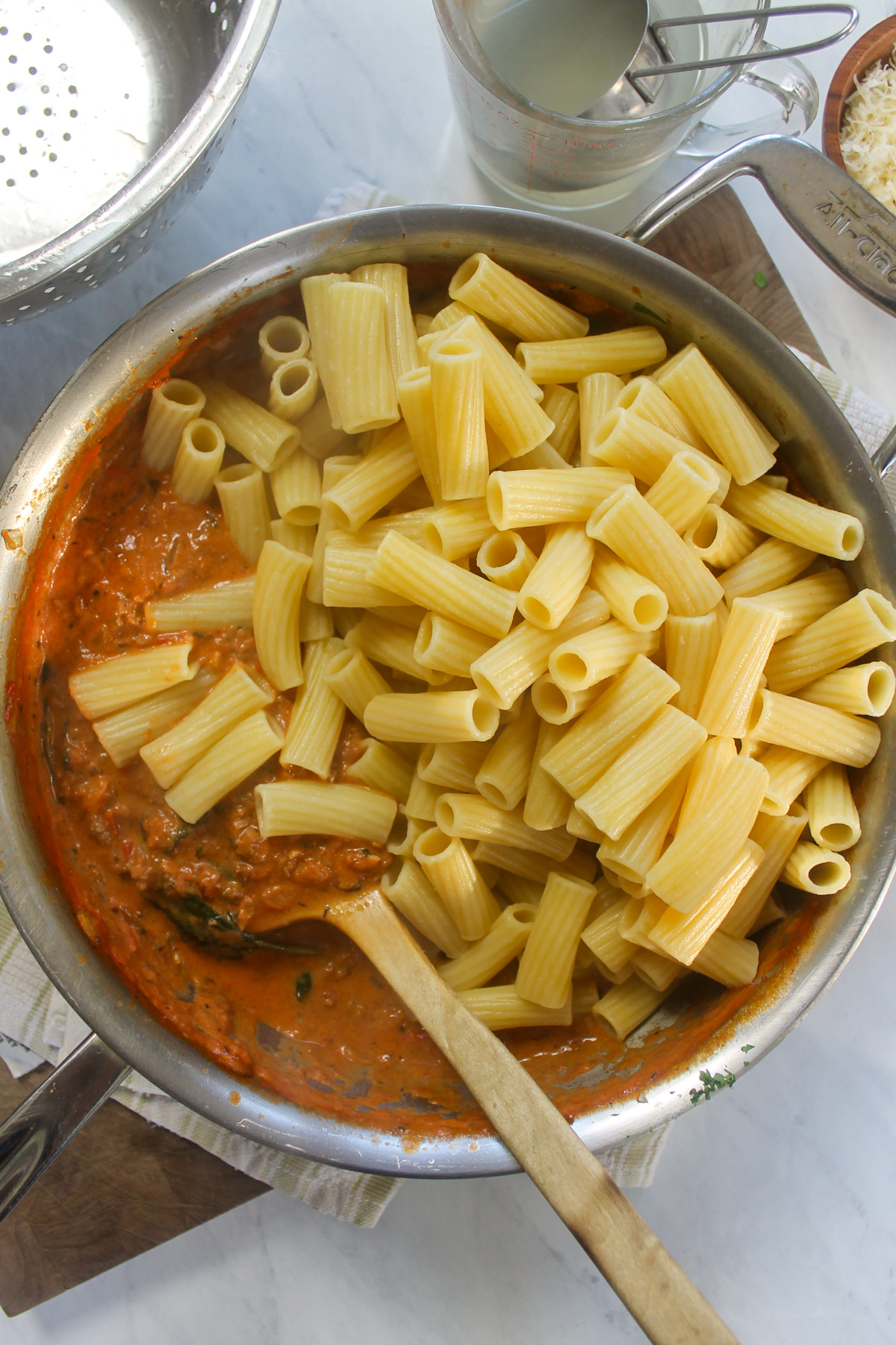 Adding cooked rigatoni to the skillet of red sauce.