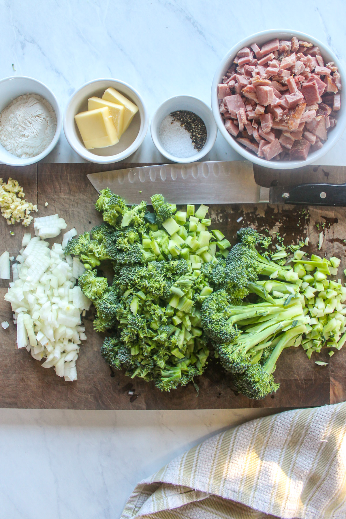 Chopped onion and broccoli on a cutting board with a bowl of chopped ham.