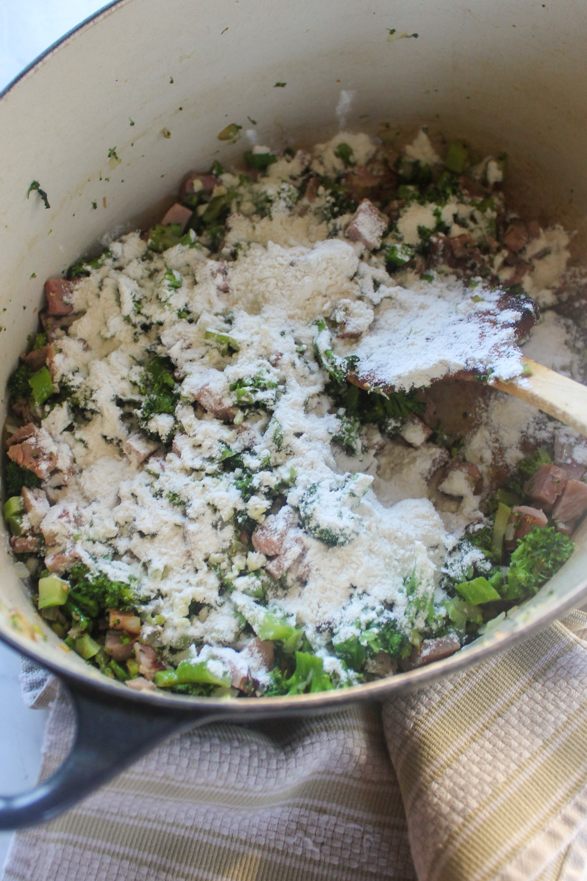 Adding flour to a soup pot with broccoli and ham.