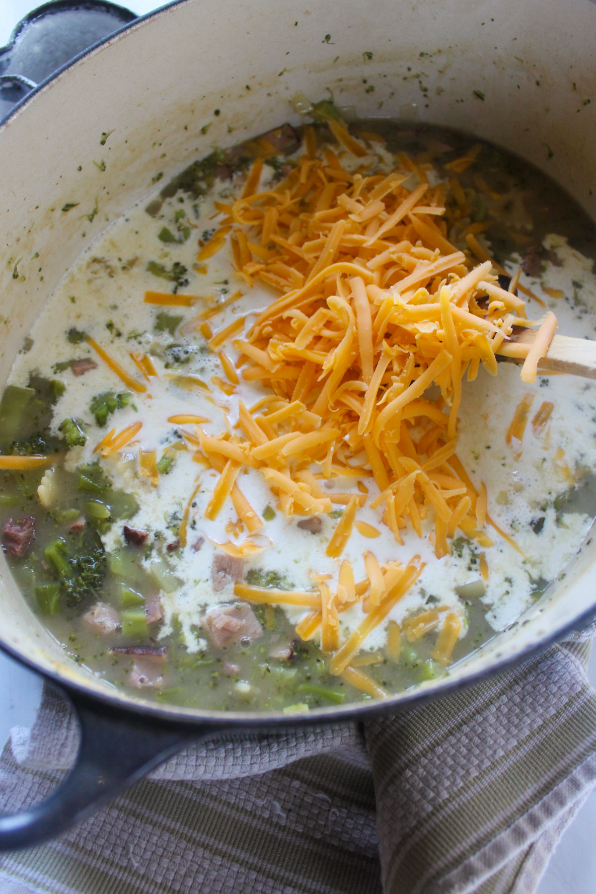 Adding cream and shredded cheddar cheese to soup.