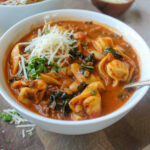 A bowl of tomato based tortellini soup with Parmesan cheese.