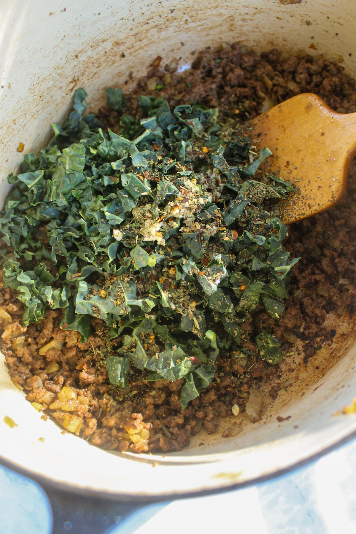 Adding chopped kale, garlic and spices to ground beef in a soup pot.