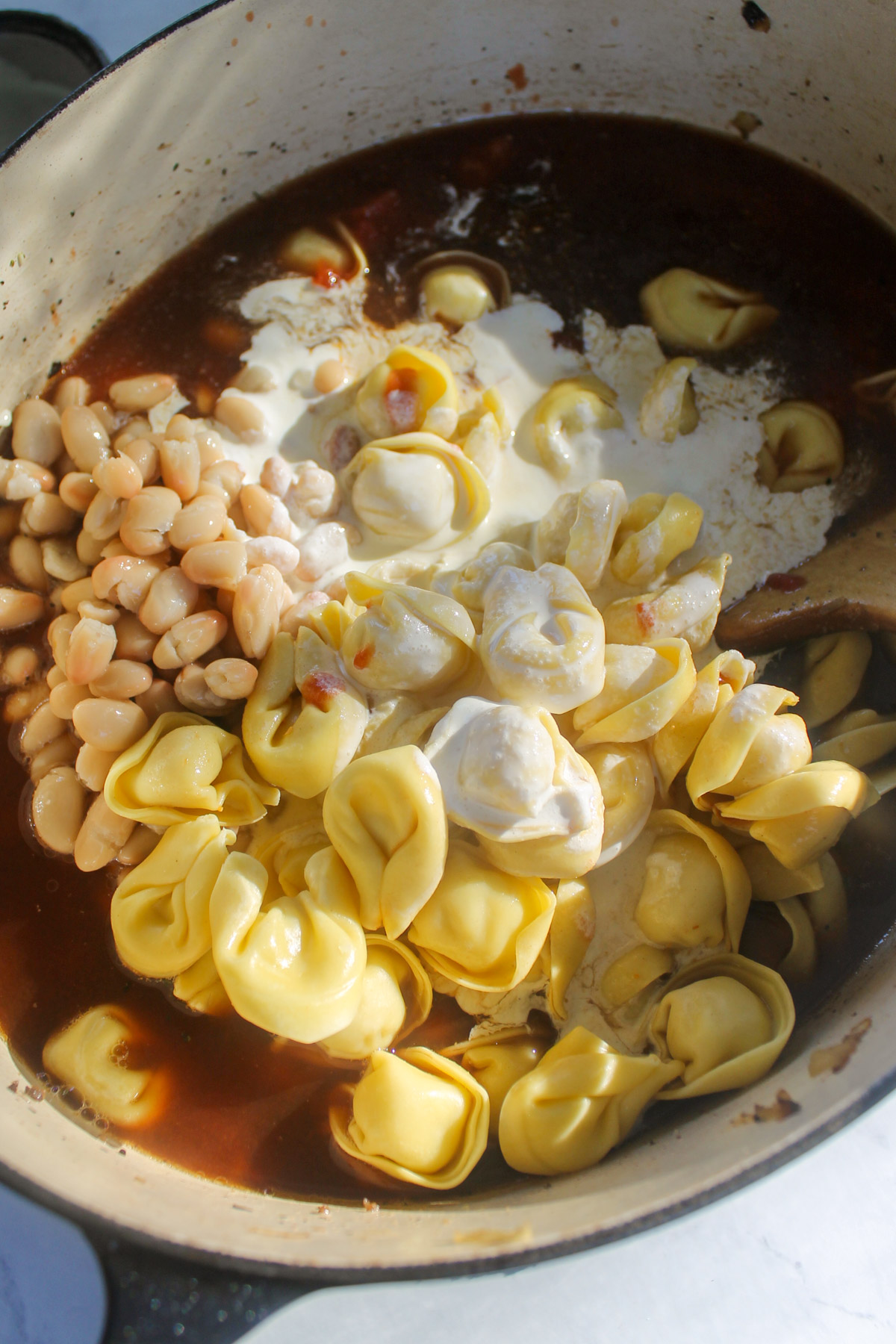 Adding tortellini, white beans, tomato and cream to the soup.