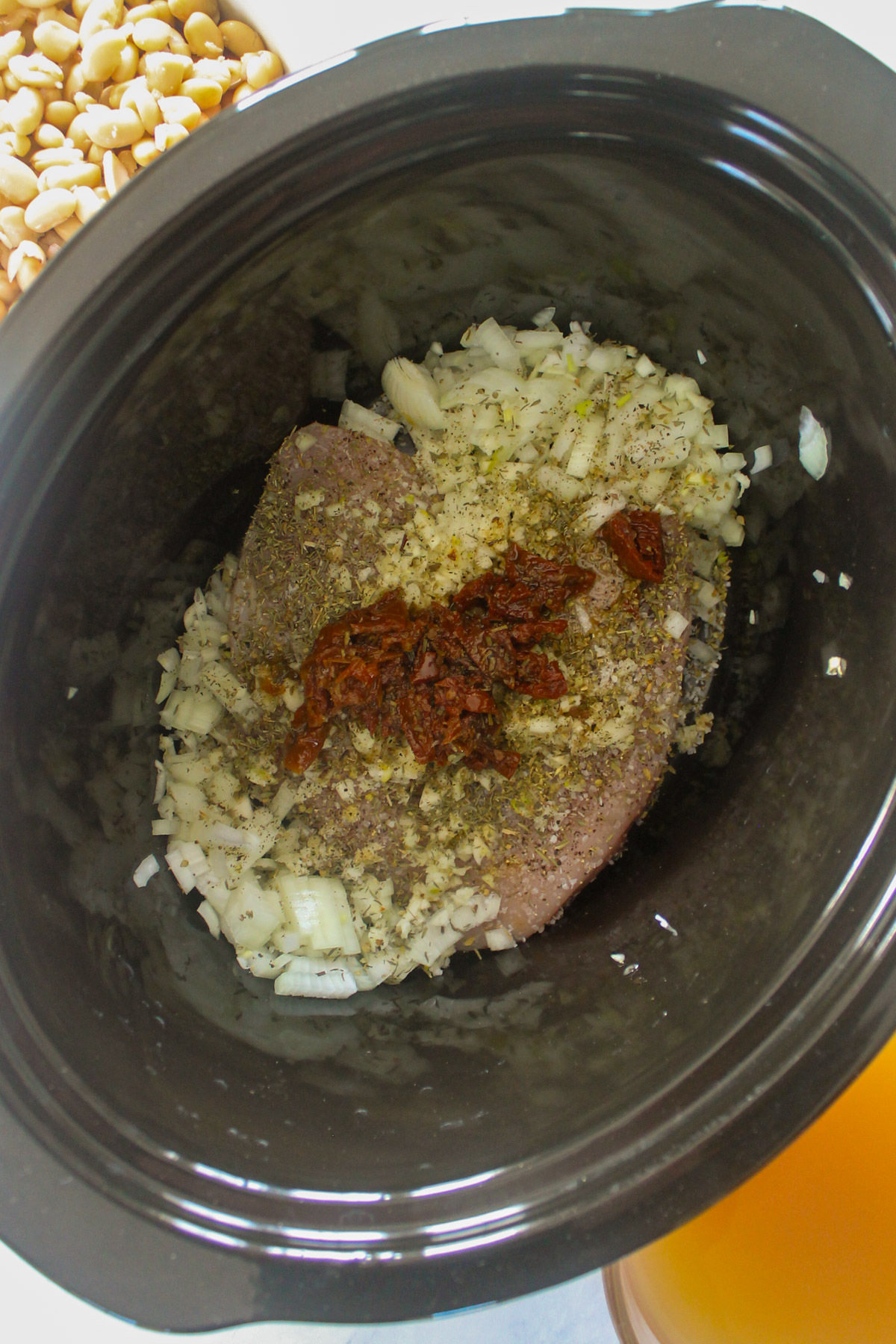 Raw chicken in a crockpot with seasonings, onions, garlic and sun-dried tomatoes.